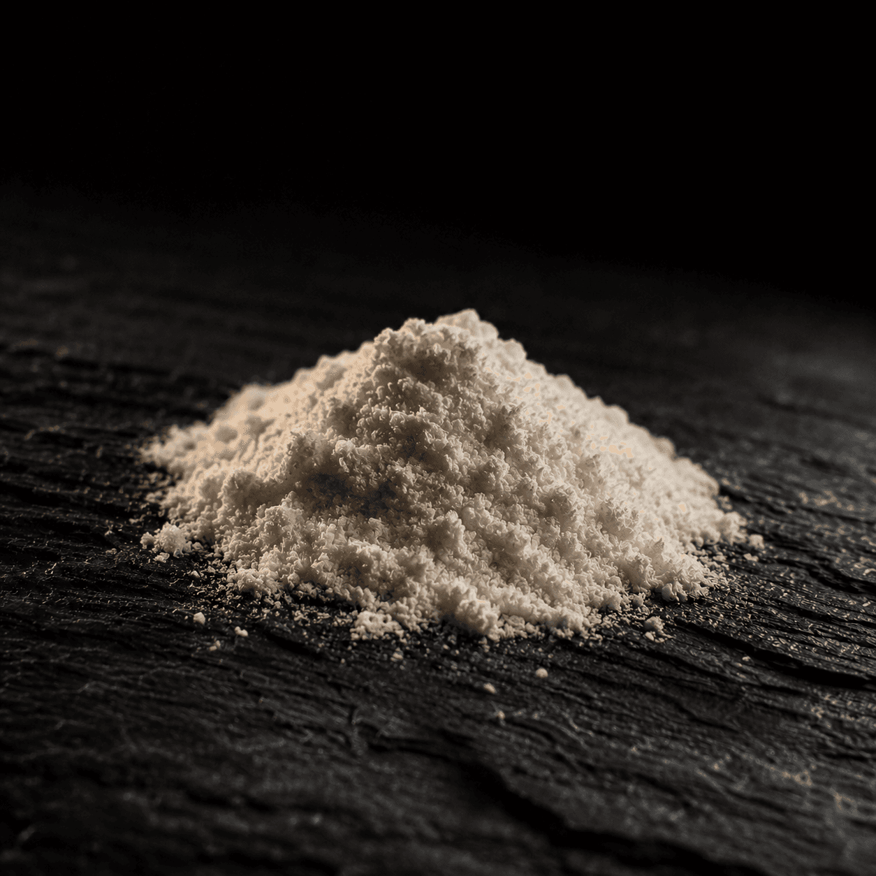 Macro shot of fine off-white magnesium bisglycinate powder on dark charcoal wood