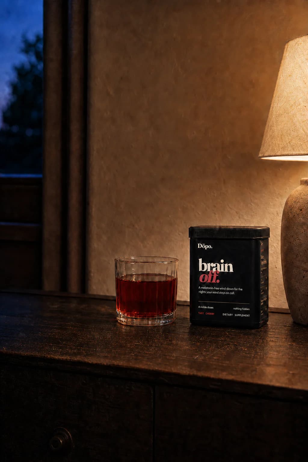 Pre-production concept render of the black Dōpo Brain Off tub beside a ruby nighttime drink on a dark nightstand