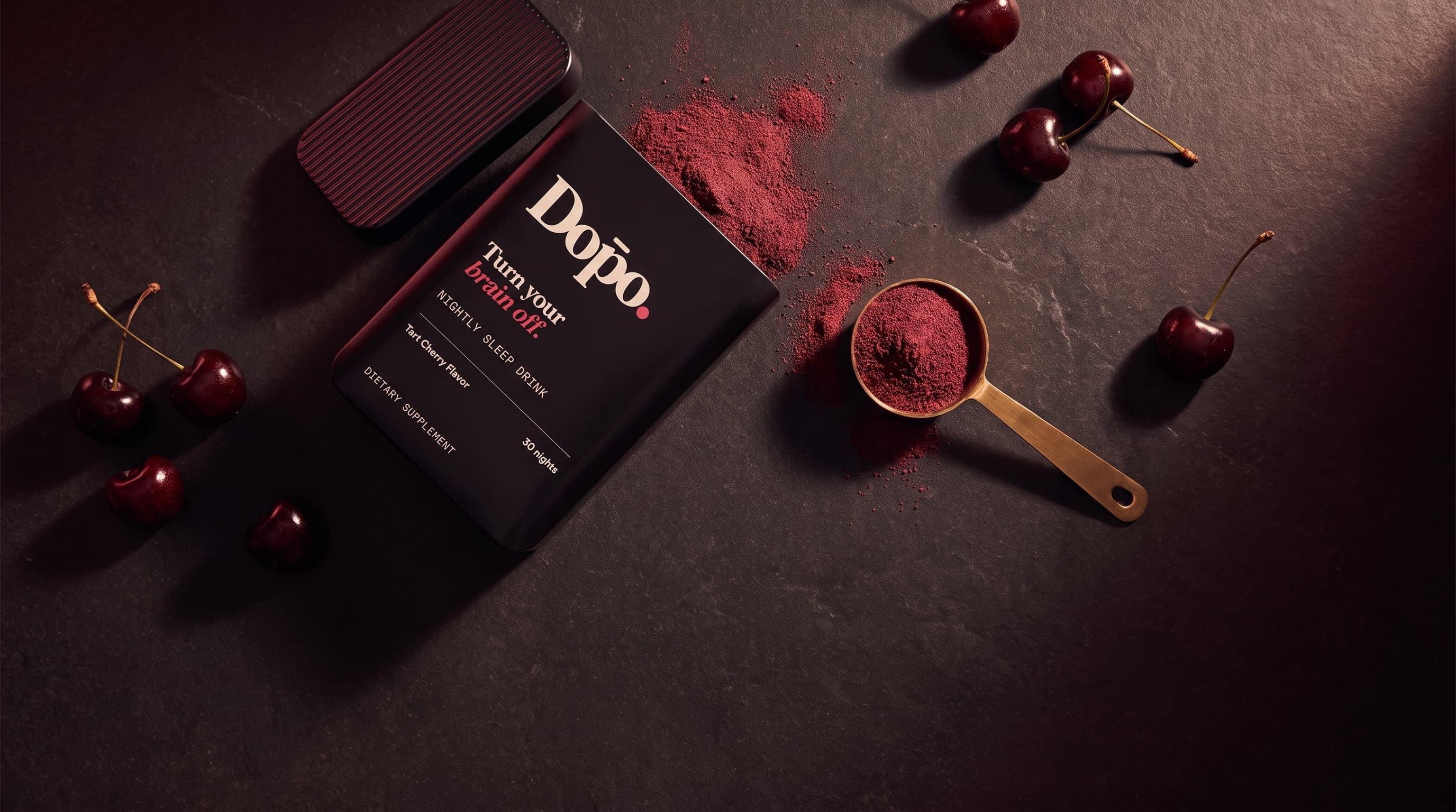 Open Dōpo tin and brass scoop of tart cherry powder on a dark surface.